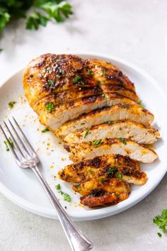 a white plate topped with sliced chicken and garnished with parsley next to a fork