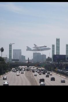 an airplane is flying over the highway in front of some tall buildings and palm trees