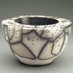 a white and black vase with designs on it's sides, sitting on a gray surface