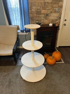 three tiered cake stand in front of a fireplace with pumpkins on the floor