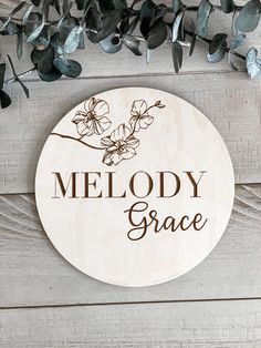 a wooden sign that says melody grace with flowers and leaves around it on a wood background