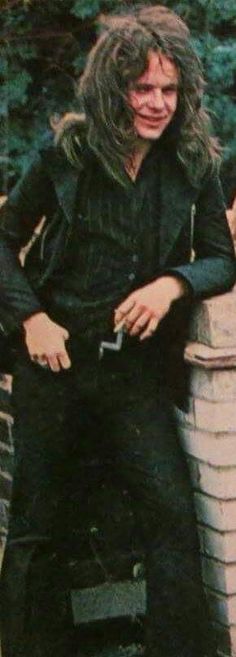 a man with long hair sitting on top of a brick wall