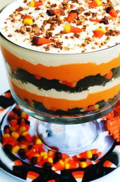 a layered halloween dessert with candy corn and whipped cream in a glass trifle dish