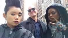 two men and a woman posing for a photo in front of tall buildings with their fingers up