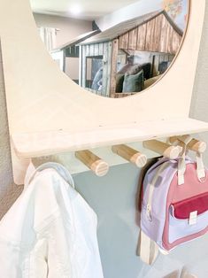 a mirror hanging on the wall next to a coat rack and purse with clothes in it