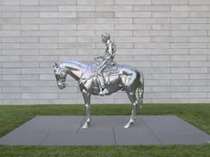 a statue of a man riding on the back of a silver horse in front of a brick wall