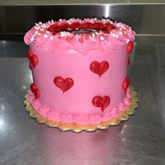 a pink cake with hearts on it sitting on top of a metal table in a kitchen