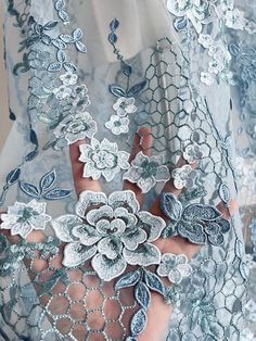 a close up of a person's hand wearing a lace dress with flowers on it