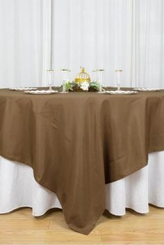 the table is covered with a brown cloth and white linens as well as candles