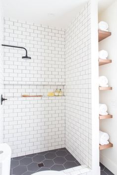 a white tiled bathroom with shelves and toilet