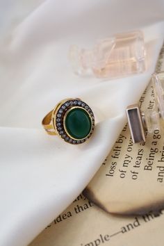 This elegant ring features a central green stone surrounded by sparkling cubic zirconia, adding a touch of glamour to any ensemble. Its versatility makes it perfect for complementing a variety of outfits and styles. Finish: 22KT Gold Plating Material: Silver, Copper Alloy, Polki Color: Green Size: One Size Closure Type: Adjustable Box Contains: 1 Ring Green Rings With Diamond Accents, Green Diamond May Birthstone Rings, Luxury Green Diamond Open Ring, Jeweled Diamond Rings, Diamond Jeweled Rings, Luxury Green Crystal Ring With Gemstone, Fine Jewelry Green Diamond Ring With Gemstone Accents, Diamond Rings With Jeweled Details, Elegant Crystal Open Ring With Stones