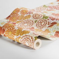 a roll of toilet paper on top of a flowered wallpaper covered in orange and pink flowers