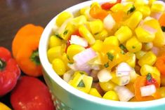 a bowl filled with corn and vegetables next to some red bell peppers on the table