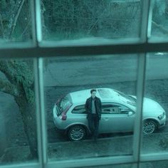 a man standing next to a parked car in front of a window on a rainy day