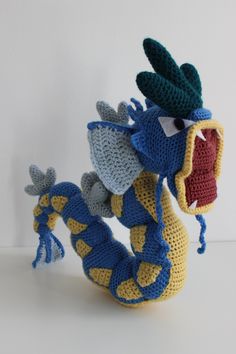 a crocheted toy dragon with its mouth open and teeth wide open, sitting on a white surface