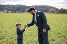 a man in a suit and tie holds the hand of a boy in a field