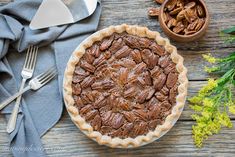 a pecan pie sitting on top of a wooden table next to a knife and fork