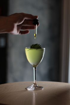 a person is pouring something into a small glass filled with liquid on top of a table