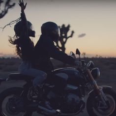 a man and woman riding on the back of a motorcycle in front of a desert landscape