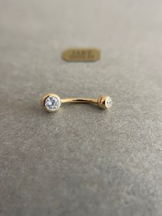 a gold nose ring with a single diamond on it's end, sitting on a gray surface