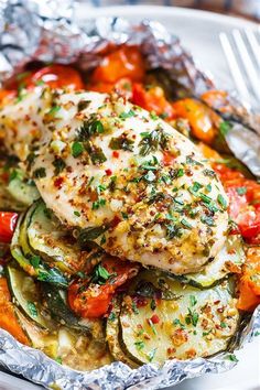 chicken, zucchini and tomatoes in foil on a white plate with a fork