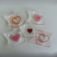 four square glass coasters with different colored hearts in them on a white table top