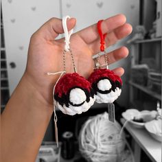 a hand holding two small red and white ball shaped keychains in front of a table