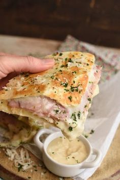 a person is holding up a sandwich on a cutting board with dipping sauce in it