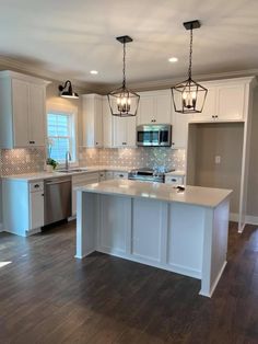 an empty kitchen with white cabinets and wood flooring, lights hanging from the ceiling