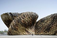 a person standing in front of a large sculpture made out of wooden planks and logs