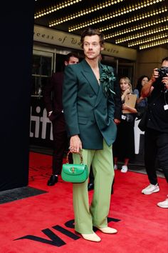 a man in a green suit and matching shoes poses on the red carpet at an event