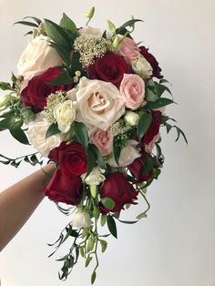 a bridal bouquet with roses and greenery is held by someone's hand