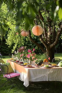 a table set up for a party with paper lanterns hanging from the trees and flowers