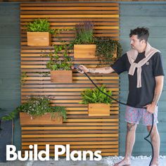 a man is using a hose to water plants on the side of a building with vertical wood slats