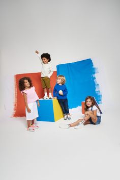 three children standing on top of colorful blocks in front of a white background with blue, yellow and red paint