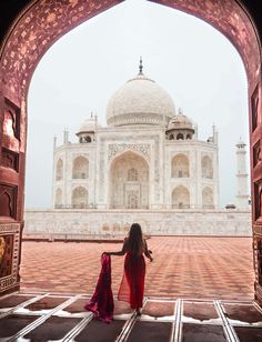 a woman in a red dress is walking towards the tajwa mosque, india