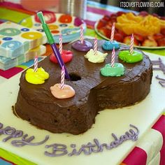 a birthday cake with chocolate frosting and lit candles on it, surrounded by other colorful candies