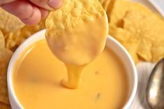 a hand holding a tortilla chip over a white bowl filled with cheese dip