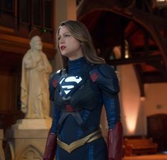 a woman in a superman costume standing next to a bust - sized statue and looking off into the distance