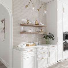 a white kitchen with gold accents and open shelving on the wall, along with wooden flooring