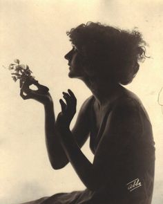 a black and white photo of a woman with flowers in her hand, sitting on the ground