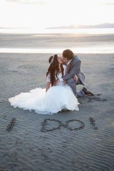 a bride and groom kissing on the beach in front of the word love written in the sand