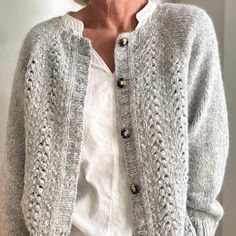 an older woman wearing a white shirt and cardigan sweater standing in front of a wall