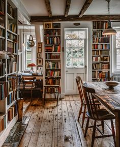 a room filled with lots of books next to a table and chairs in front of a window