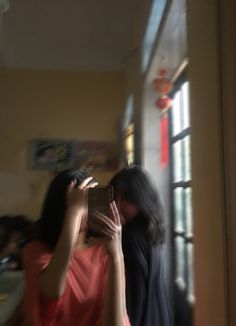 two women standing in front of a window looking at their cell phones and taking pictures