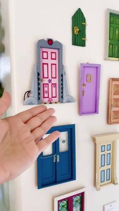 a hand is reaching for magnets on a refrigerator door that are decorated with miniature houses and doors