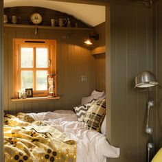 a bed sitting under a window next to a yellow chair in a room with wooden walls