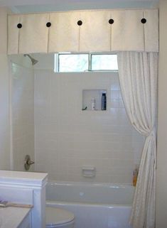 a white bath tub sitting under a window next to a toilet and shower head mounted on a wall