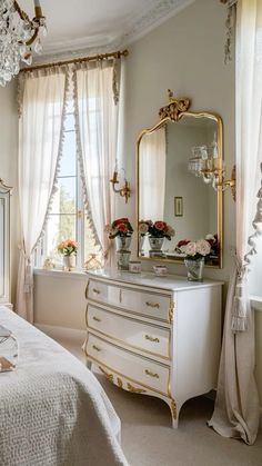 a white dresser sitting in front of a window next to a bed and a chandelier