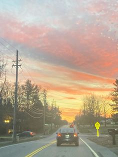 a car is driving down the road at sunset or dawn with pink clouds in the sky